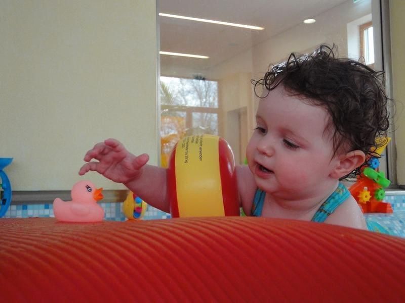 Baby greift nach Quietsche-Ente am Beckenrand